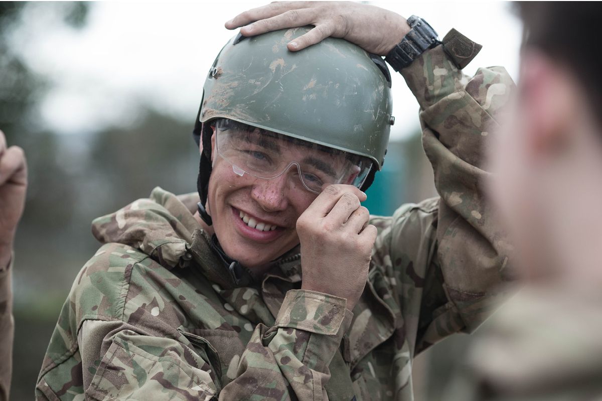 A smiling Royal Marines Cadet adjusting his helmet